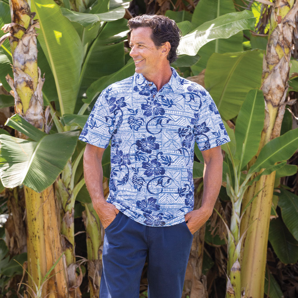 Man wearing a blue floral shirt standing among tropical plants
