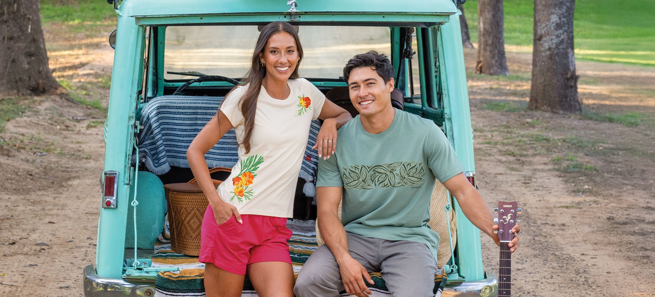 Two people standing in front of a vintage van with a guitar, outdoors.