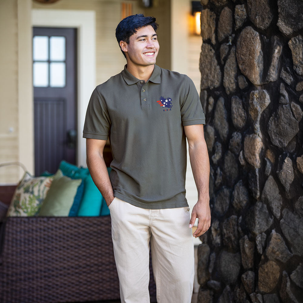 Man wearing a green polo shirt with a logo standing in front of a stone wall.