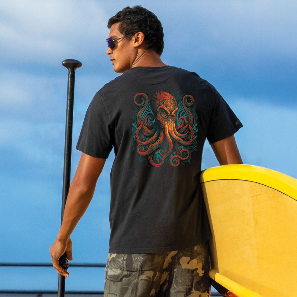 Man holding a yellow paddle board with an octopus design on his black t-shirt against a blue sky.