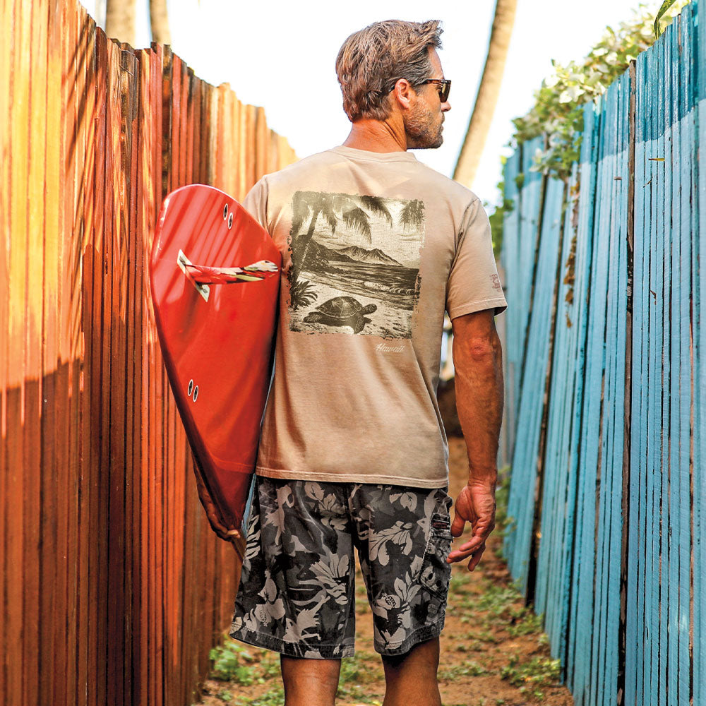 Man holding a red surfboard with a wooden and blue fence in the background